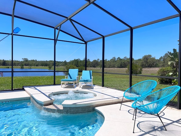 Relax by the pool surrounded by lush greenery and a serene body of water.