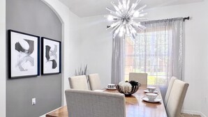 A dining area with a wooden table, four chairs, a chandelier, and two framed artworks on the wall.