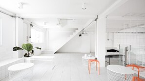 Un interior moderno y blanco con una escalera, mesas redondas y sillas naranjas.