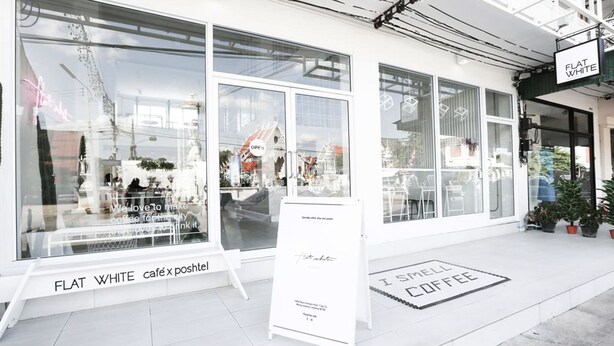 Una cafetería con grandes ventanales y un letrero que dice "FLAT WHITE café x poshtel".