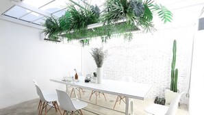 Una sala de reuniones moderna con una mesa y sillas blancas, y plantas colgantes.