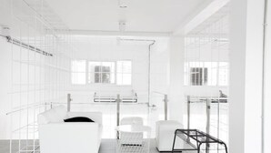 Una habitación moderna y minimalista con un sofá blanco, una mesa redonda y un banco de metal.