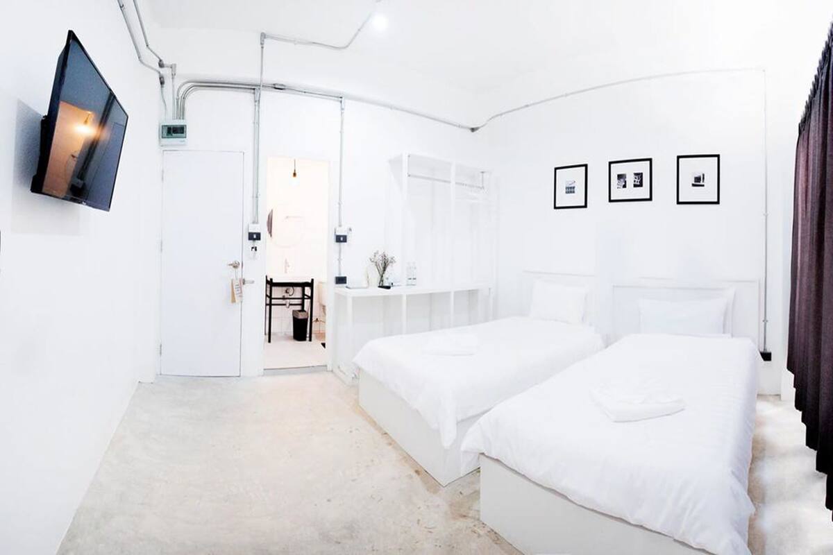 Ein modernes Hotelzimmer mit zwei Betten, einem flachbildfernseher an der Wand und einem kleinen Schreibtisch mit Stuhl.