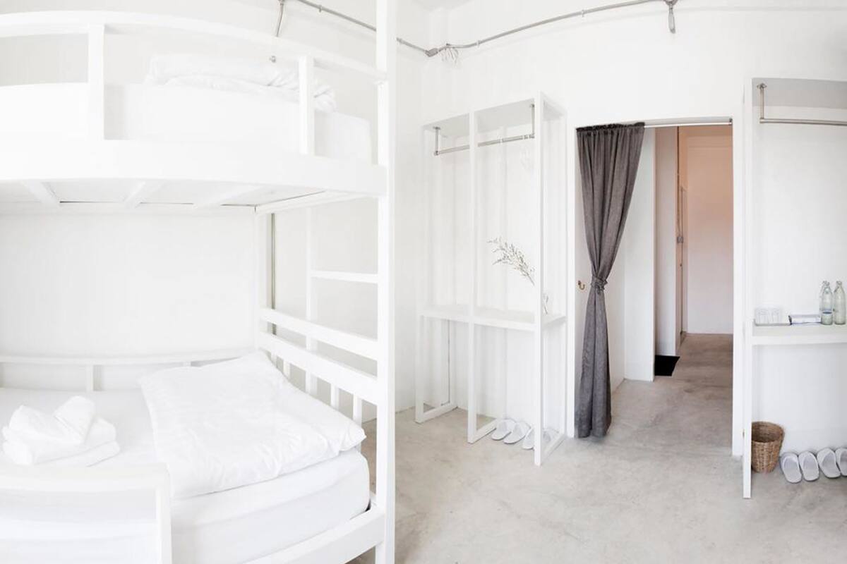 Ein weißes Zimmer mit Etagenbetten, einem kleinen Tisch und einem Ablagefach mit Pflegeartikeln.