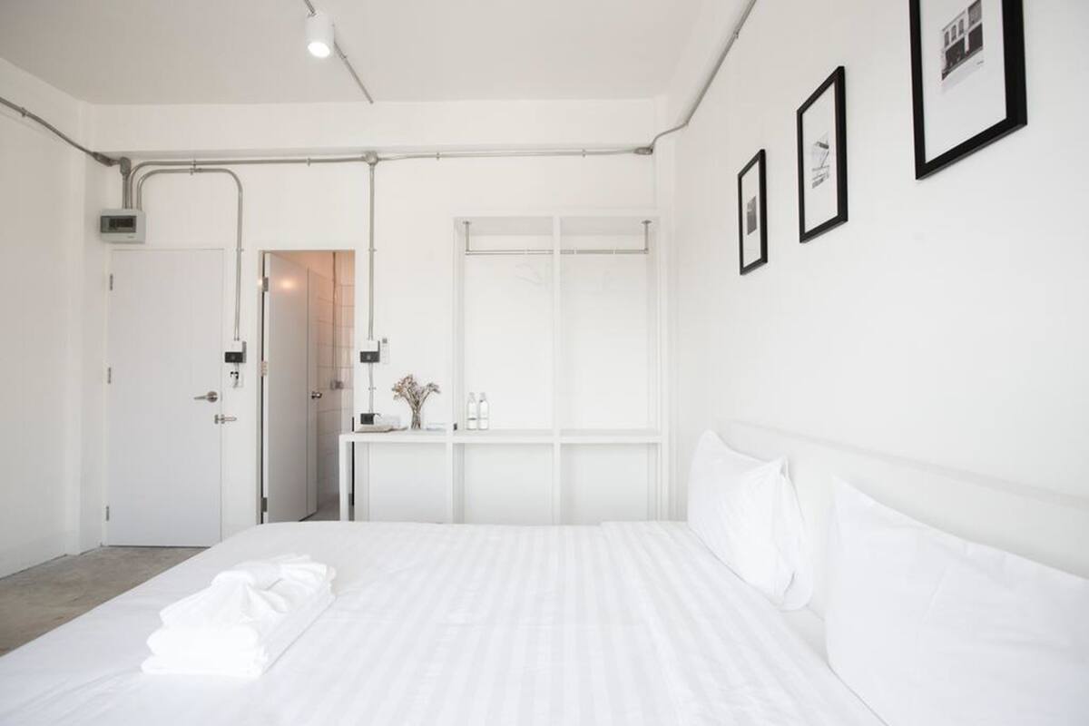 Ein Hotelzimmer mit einem ordentlich bezogenen Bett, einem Fenster mit Jalousien, einer Tür und einer Wand-Klimaanlage.