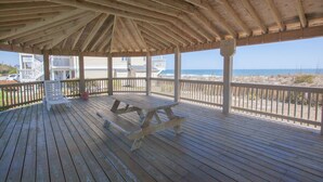 Una terraza de madera con una mesa de picnic y una silla, con vistas a una playa y al océano.