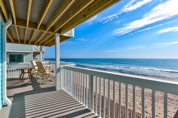 A wooden deck with a view of the ocean, a table, and two chairs.