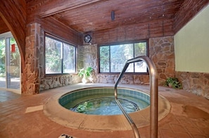 An indoor hot tub area with stone walls, wooden ceiling, and large windows.