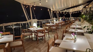 Een buitenterras met tafels, stoelen, lichtslingers en plantenpotten.