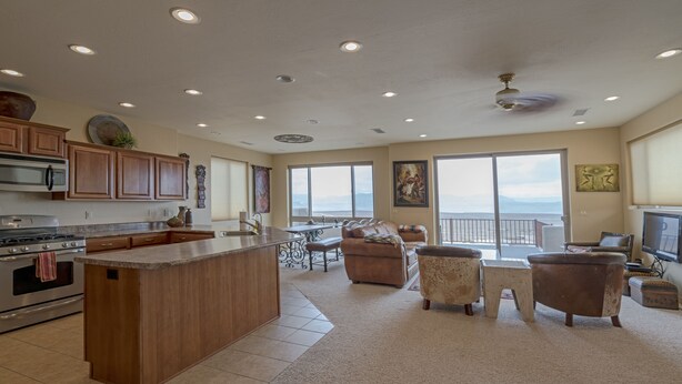 Cocina amplia con una isla grande, armarios de madera y vistas al exterior. Cuenta con un comedor con mesa y sillas, además de una sala de estar con sofá y televisor.