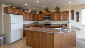 Una cocina con gabinetes de madera, una isla central, un refrigerador, una estufa y un microondas.