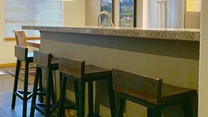 Una cucina con angolo bar, sgabelli di legno, un frigorifero e una finestra con persiane.