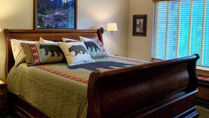 Una camera da letto con un letto in legno, una ventola a soffitto, un quadro, una finestra con persiane e una lampada.