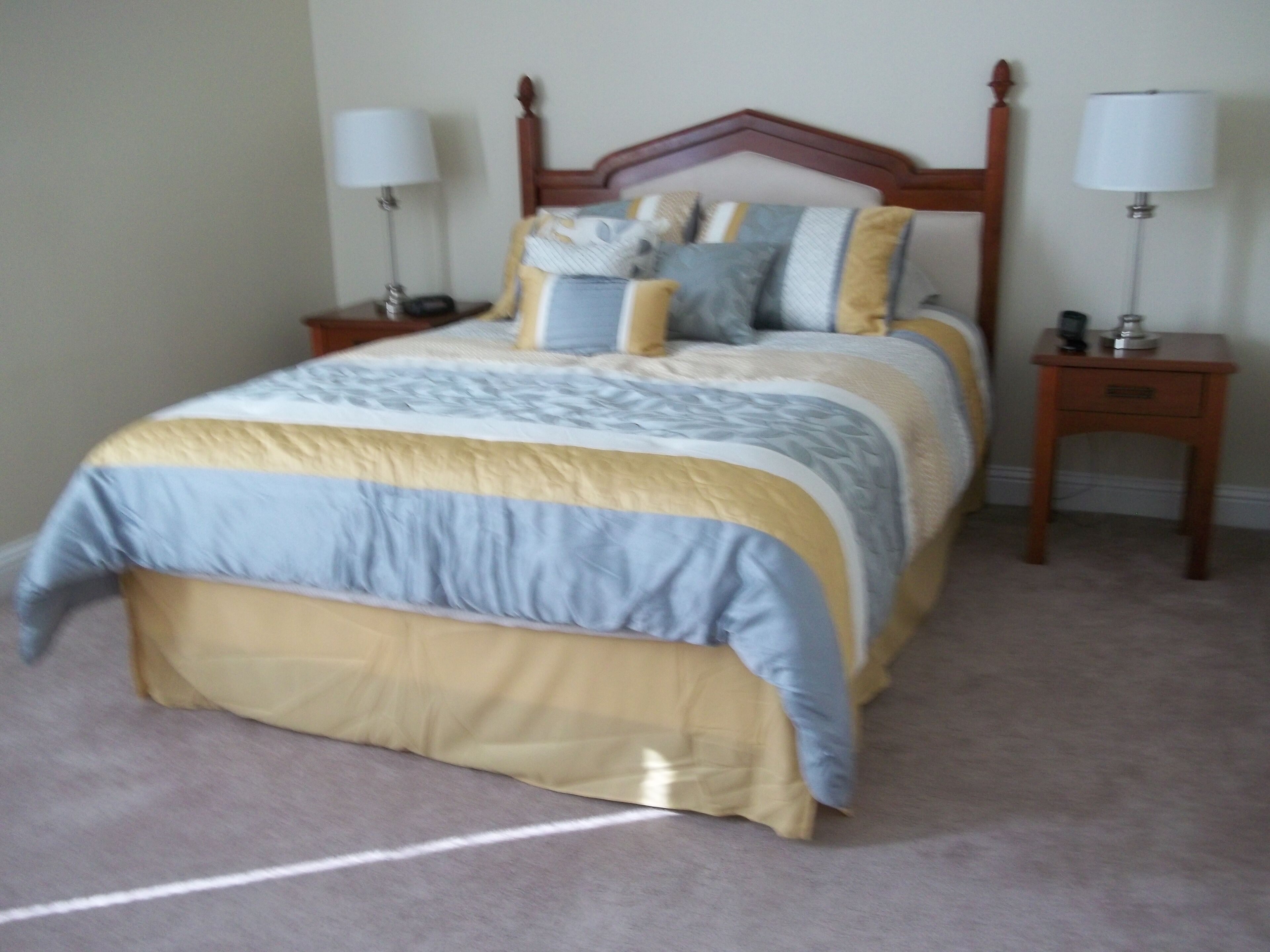 A neatly made bed with a wooden headboard, two bedside tables with lamps, and a carpeted floor.