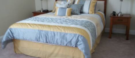 A neatly made bed with a wooden headboard, two bedside tables with lamps, and a carpeted floor.