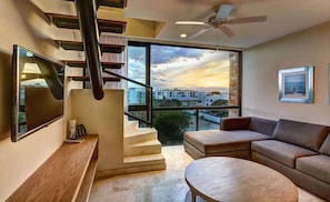 Ein modernes Wohnzimmer mit Treppe, großem Fenster mit Stadtblick, Flachbildfernseher und Deckenventilator.