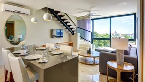 A modern dining area with a central island, a staircase, a sofa, and a large window with a view. - Central Penthouse, Private Roof & Pool, Gym, 402 (Playa del Carmen)