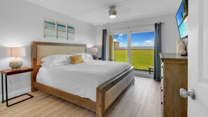A bedroom with a large bed, a TV mounted on the wall, and a view of the outdoors. - Ocean Front 2 Bed 2 Bath With Ocean Front Pool, walk to restaurants (St. Augustine)