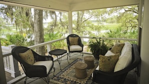 Un porche cubierto con muebles de mimbre, vista a un lago y árboles con musgo español.