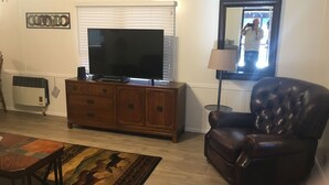 A living room with a flat-screen TV on a wooden cabinet, a leather armchair, a patterned rug, and a mirror on the wall. - WW, Kentucky Lake, Bass Fish, Nashville, MEMPHIS, Birdsong Marina, Paris Landing (Camden)