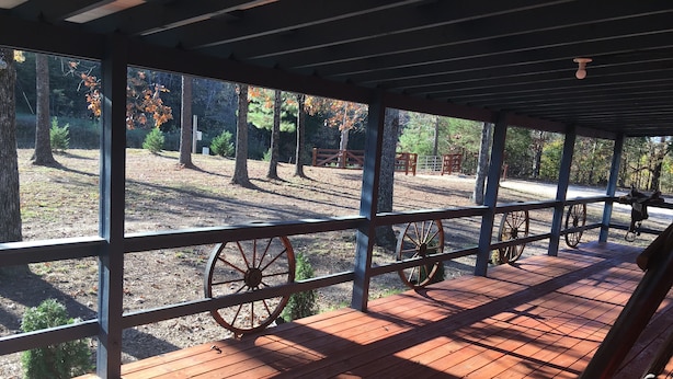 A covered wooden deck with a view of a forested area, featuring a rustic wheel and a small bench. - WW, Kentucky Lake, Bass Fish, Nashville, MEMPHIS, Birdsong Marina, Paris Landing (Camden)