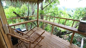 A wooden deck with a bamboo railing, surrounded by lush greenery. - Cast Away  Homestay (Pak Kret)