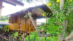 A wooden treehouse with a thatched roof, built on a tree trunk, featuring a small balcony and a staircase leading to the entrance. - Cast Away  Homestay (Pak Kret)