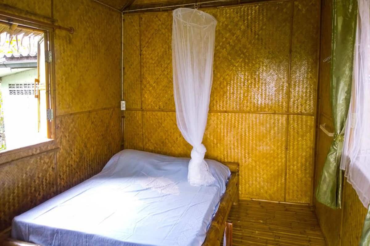 A small, single-bed room with a mosquito net over the bed and a window on one side.