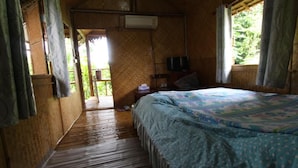 A room with a bed, a small table, a chair, and a TV. There is a window with curtains and a door leading to an outdoor area. - Cast Away  Homestay (Pak Kret)