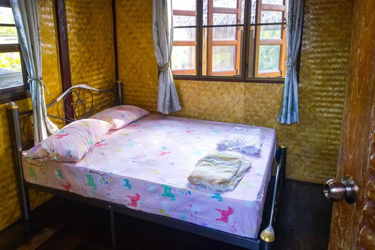 A single bed with a floral bedspread, a metal frame, and a wooden door.