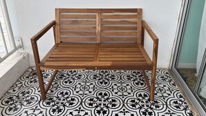 Un banco de madera con respaldo y reposabrazos, sobre un piso de baldosas estampadas.