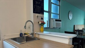 Una cocina con un lavamanos de acero inoxidable, una encimera de madera, un florero con flores, un reloj y una ventana con persianas.