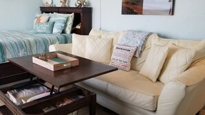 A cozy room with a bed, a beige sofa, a wooden coffee table, and a small wooden chest. - Salty Kisses OCEANFRONT Daytona Beach studio condo (Daytona Beach)