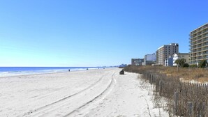 Una playa con un camino de arena que conduce a un edificio con varios pisos y balcones.