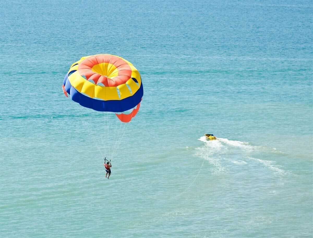 Un pratiquant de parachute ascensionnel, équipé d’un parachute aux couleurs vives, survole une étendue d’eau calme.