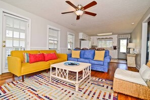 A living room with a yellow sofa, blue sofa, and a white coffee table. - Decked Out Ocean Inlet House Private Pool Tiki Hut (North Myrtle Beach)