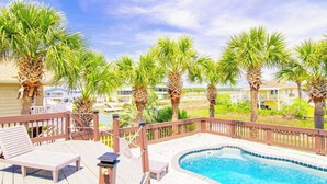 Un área de piscina con terraza de madera, sillas de descanso y palmeras.