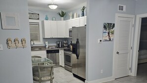 A modern kitchen with white cabinets, stainless steel appliances, and a dining area with a wooden table and chairs. - Island Retreat: Resort Condo Offering Oasis Pool and Inviting Tiki Bar (Pensacola)
