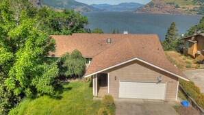 A house with a garage, surrounded by lush greenery and a view of a lake and mountains. - Amber Sunset - Views! Spacious, Light Bright, Gorge-ous Views! (Mosier)