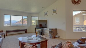 A living room with a large window, a flat-screen TV, a fireplace, and a bench. - Amber Sunset - Views! Spacious, Light Bright, Gorge-ous Views! (Mosier)