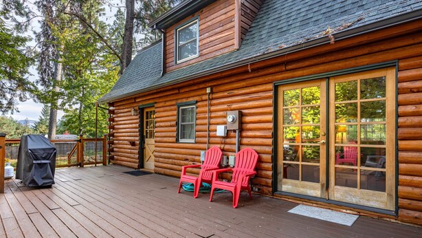 Een blokhut met een terras, twee rode Adirondack-stoelen, een grill en een overdekte barbecueplek.