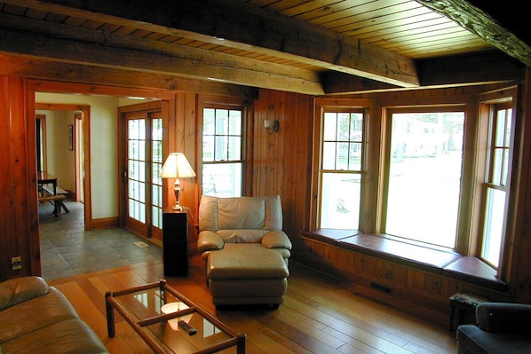 A cozy room with wooden walls, a cushioned armchair, a small table, and large windows.