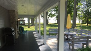 A covered patio area with a grill, benches, and an umbrella. - Beautiful Lake House, 6 BR, 5 BA, 3500 SF, private beach, wrap around porch. (Fort Erie)
