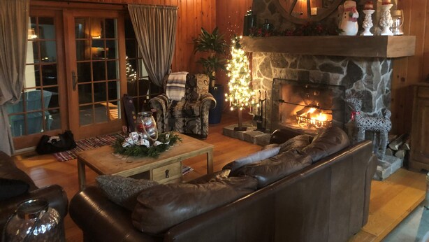 A cozy log cabin interior with a stone fireplace, leather sofa, and a Christmas tree. - Beautiful Lake House, 6 BR, 5 BA, 3500 SF, private beach, wrap around porch. (Fort Erie)