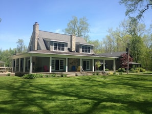 A two-story house with a stone chimney, a covered porch with multiple windows, and a well-maintained lawn.