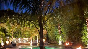 Un espace extérieur avec piscine, aménagé pour la nuit, comprenant une piscine bien éclairée, des chaises longues et un foyer.