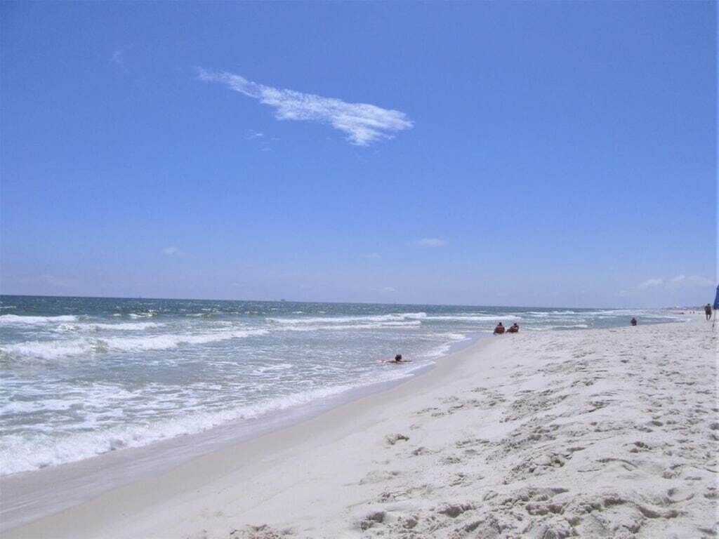 A beach with a clear sky, sandy shore, and a few people in the distance.