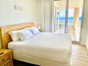 Una camera d'albergo con una testiera in legno, un letto grande con lenzuola bianche, un comodino e vista sul balcone e sull'oceano.