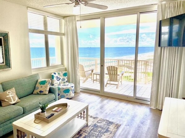 Un soggiorno con vista sull'oceano, una ventola a soffitto e un balcone con mobili da esterno.