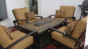 A patio with four chairs and a table, white siding walls, and a door.